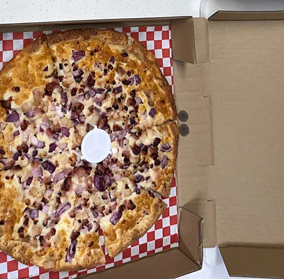Pizza topped with red onions and meat in an open box on a red-checked liner