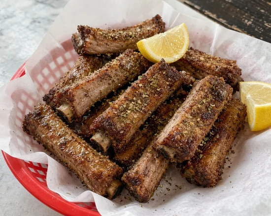 Greek dry ribs seasoned with salt, pepper and oregano, with lemon wedges in a paper-lined basket